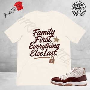 May include: Cream-colored t-shirt with the text "Family First, Everything Else Last" in brown script. A star and a lock graphic are included. A pair of white and brown high-top sneakers are in the image.
