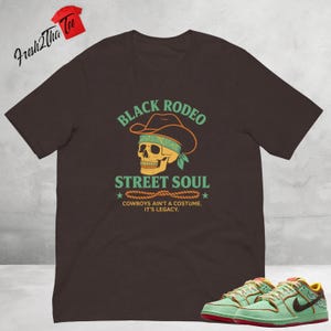 Può includere: Una maglietta marrone con il testo "BLACK RODEO STREET SOUL" e le parole "COWBOYS AIN'T A COSTUME. IT'S LEGACY."  Un teschio con un cappello da cowboy è presente sulla maglietta.