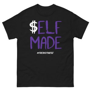 May include: Black t-shirt with the text "$ELF MADE" in white and purple. The dollar sign is white, and the rest of the text is in a handwritten style. The hashtag #FRESH2THATEE is below the text.