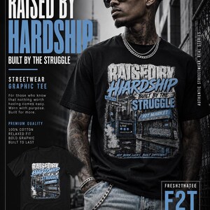 以下が含まれることがあります： 「RAISED BY HARDSHIP BUILT BY THE STRUGGLE」および「NOT BORN LUCKY, BUILT DIFFERENT」というテキストがプリントされた、黒の半袖Tシャツ。デザインには「F2T MARKET」と書かれた店舗の正面と地下鉄の入り口が描かれています。