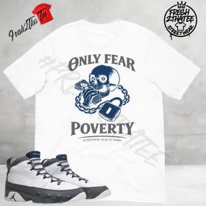May include: White t-shirt with a navy blue skull graphic, chains, and padlock, with the text "ONLY FEAR POVERTY". Below are white and gray high-top sneakers with navy blue accents. The shirt has the Fresh 2 Tha Tee logo.