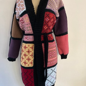 May include: A long, black cardigan with a patchwork design. The cardigan is made of different colored squares of yarn, including red, pink, purple, brown, and beige. The cardigan has a V-neck and a tie belt.