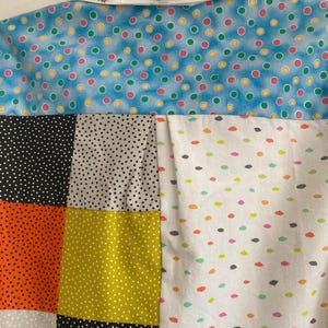 May include: A patchwork shirt with a white collar and a variety of colorful polka dot patterns. The shirt has a blue, black, white, orange, and yellow polka dot pattern.