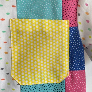 May include: A patchwork fabric with a yellow pocket. The fabric is made of different colored polka dot patterns in blue, pink, green, and white.