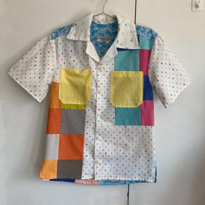 May include: A short-sleeved button-down shirt with a patchwork design. The shirt is made of different fabrics with various patterns, including polka dots, stripes, and floral prints. The shirt has a white background with colorful patches.