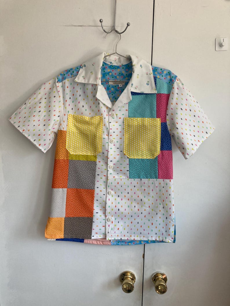 May include: A short-sleeved button-down shirt with a patchwork design. The shirt is made of different fabrics with various patterns, including polka dots, stripes, and floral prints. The shirt has a white background with colorful patches.