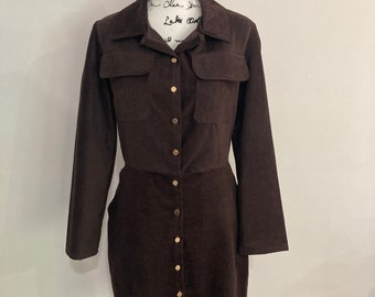 May include: A brown corduroy dress with a collared neckline, long sleeves, and a button-up front. The dress has two flap pockets on the chest and a fitted silhouette.