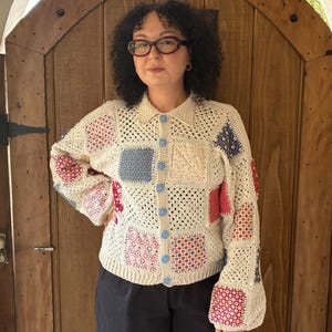 May include: A long-sleeved crochet cardigan featuring a patchwork design of cream-colored openwork squares interspersed with various floral and geometric patterned fabric squares. The garment has a collared neckline and five light blue buttons.