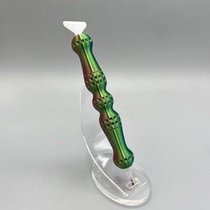 May include: A green, red, and white tool with a white tip and a textured handle. The tool is on a clear plastic stand.