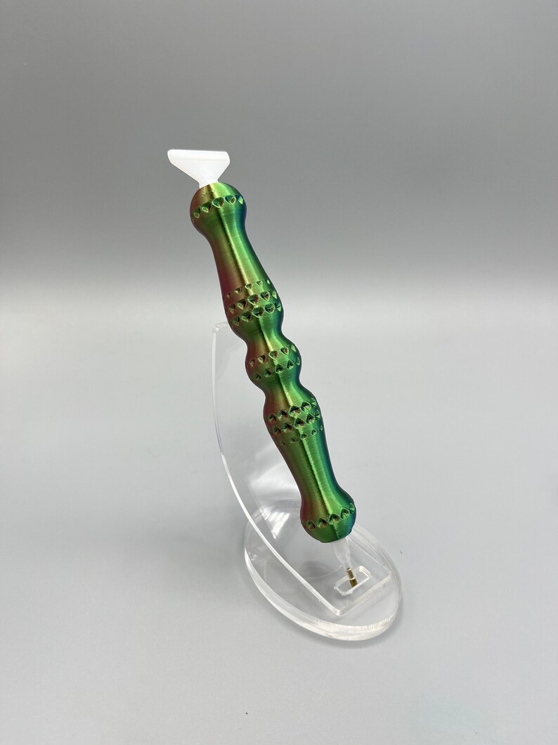 May include: A green, red, and white tool with a white tip and a textured handle. The tool is on a clear plastic stand.