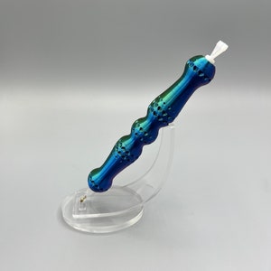 May include: A blue and green iridescent pen with a textured handle and a white tip. The pen is on a clear plastic stand.