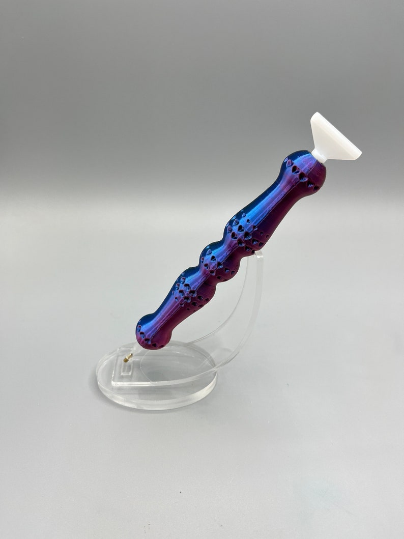 May include: A purple and blue diamond painting tool with a white tip, sitting on a clear plastic stand.