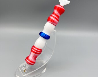 May include: A white and red striped pen with a blue ring on the handle. The pen is on a clear plastic stand.