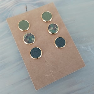 May include: Set of six round stud earrings with gold settings. The earrings feature three different patterns: solid green, camouflage, and black.