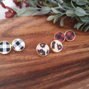 May include: A set of six small, round earrings with different patterns. Two earrings feature a black and white checkered pattern, two feature a red and black checkered pattern, and two feature a brown and beige animal print.
