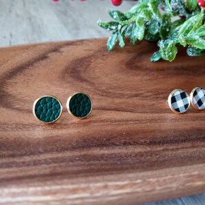 May include: Two pairs of earrings on a wooden surface. One pair is green leather and the other is black and white checkered.