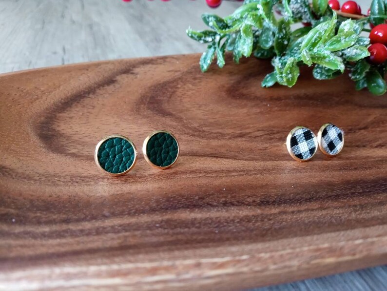 May include: Two pairs of earrings on a wooden surface. One pair is green leather and the other is black and white checkered.