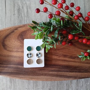 May include: A set of six small round earrings on a white card. The earrings are made of leather and have a green, black and white checkered, and brown design.