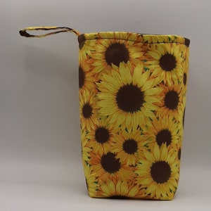 May include: A yellow and brown fabric bag with a sunflower print. The bag has a brown handle and a zipper closure.