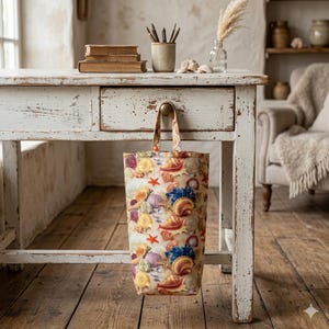 May include: A tote bag with a seashell pattern. The bag features a variety of colorful seashells, starfish, and other marine life. The bag is hanging from a white wooden desk with a drawer.