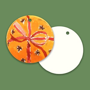 May include: Two circular gift tags with a hole at the top. One tag features an orange background with a painted red ribbon design and small dark brown star-like accents. The second tag is plain white, showing the reverse side of the circular tag.