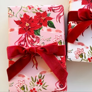 May include: Two wrapped gifts with floral wrapping paper and red velvet ribbon bows. The wrapping paper features a pink background with red poinsettias, green leaves, and other floral elements. The bows add a touch of elegance.