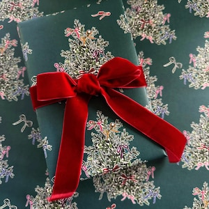 May include: A green gift wrap with a repeating pattern of Christmas trees decorated with colorful bows. A red velvet ribbon is tied around a gift box wrapped in the paper.