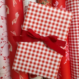 May include: A collection of red and white wrapping paper rolls with a red and white gingham gift box tied with a red ribbon.
