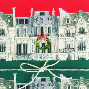 May include: A watercolor illustration of a building wrapped in green paper with a gold ribbon and a wreath with a red bow on the front.