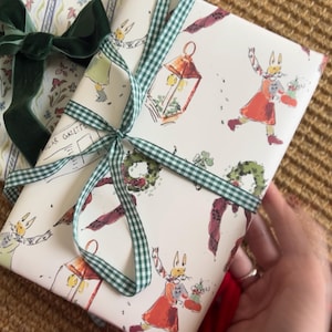 May include: Two wrapped gifts with decorative paper and bows. One gift is wrapped in floral paper with a dark green velvet bow. The other gift is wrapped in cream paper with a whimsical rabbit design and a green gingham ribbon.