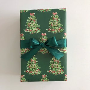 May include: A green gift box with a green ribbon and bow. The box is wrapped in paper with a repeating pattern of Christmas trees.