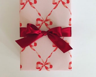 May include: A pink gift box with a red bow. The box is wrapped in paper with a repeating pattern of red bows.