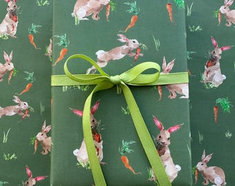 May include: Green wrapping paper with a repeating pattern of brown rabbits holding carrots. A green ribbon is tied around the paper.