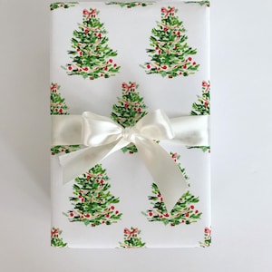 May include: White gift wrap with a repeating pattern of green Christmas trees with red ornaments and pink ribbons. A white satin ribbon is tied around the gift box.