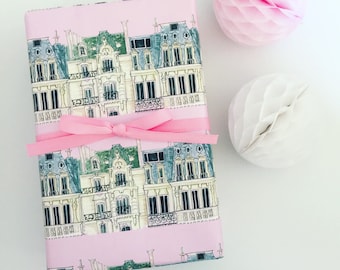 Könnte beinhalten: Rosa Geschenkpapier mit einem sich wiederholenden Muster aus illustrierten Pariser Gebäuden. Das Papier ist mit einem rosa Band gebunden.
