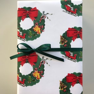 May include: A wrapped gift box featuring festive Christmas-themed wrapping paper. The paper has a white background with repeating illustrations of green wreaths, red bows, and sleighs. A dark green ribbon is tied around the box.