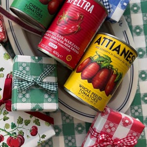 May include: An assortment of canned tomatoes and wrapped gifts. The cans are red, green, and yellow, with labels that read "Cherry Tomatoes" and "Whole Peeled Tomatoes." The gifts are wrapped in patterned paper and tied with ribbons.