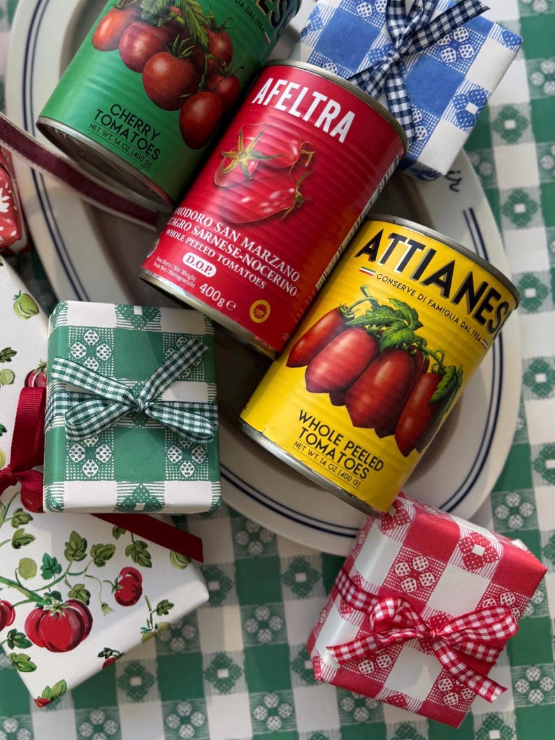 May include: An assortment of canned tomatoes and wrapped gifts. The cans are red, green, and yellow, with labels that read "Cherry Tomatoes" and "Whole Peeled Tomatoes." The gifts are wrapped in patterned paper and tied with ribbons.