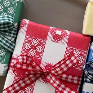 May include: Close-up of wrapped gifts with red, green, and blue gingham patterns. Each gift is tied with a matching gingham ribbon. The gifts are on a white plate with the words "grand plat" in cursive.