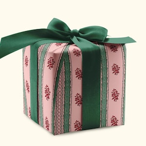 May include: A wrapped gift box with a green satin ribbon and bow. The wrapping paper is pink with a floral pattern and green vertical stripes. The box is square and sits on a cream-colored background.