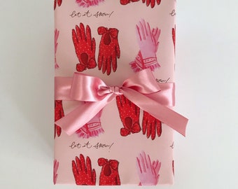 Puede incluir: Papel de regalo rosa con un patrón repetido de guantes rojos y rosas. El papel tiene el texto "Let it snow!" impreso en él.