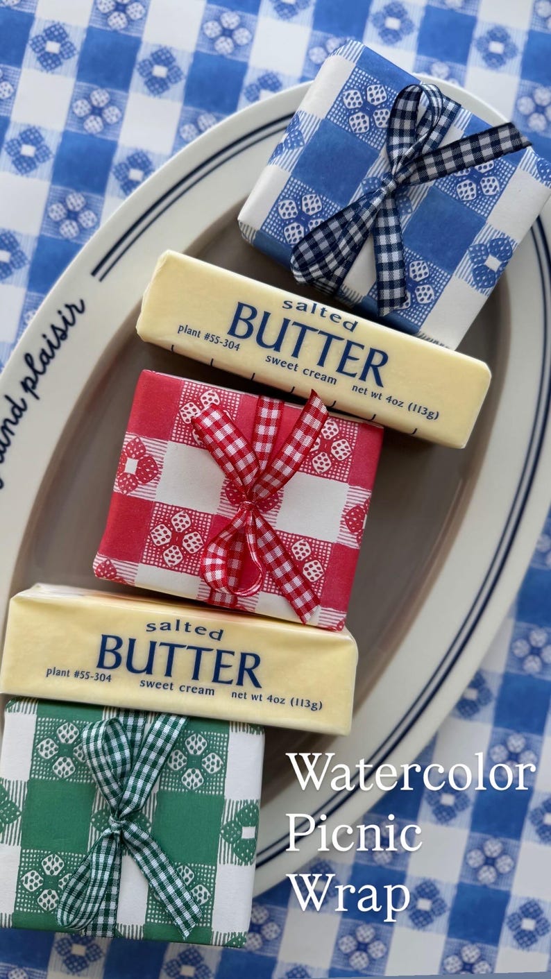 May include: Butter wrapped in watercolor picnic-themed paper. The butter is wrapped in red, blue, and green gingham patterns, tied with matching ribbons. The image includes the text "Watercolor Picnic Wrap".