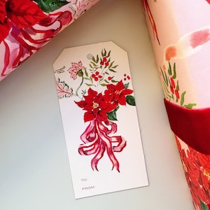 May include: A white gift tag with a red poinsettia and pink ribbon illustration. The tag has the words "To:" and "From:" printed on it.