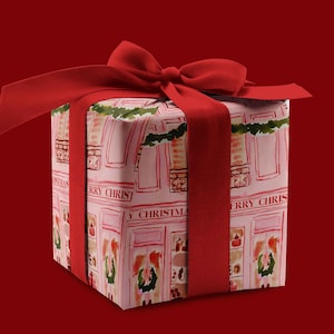 May include: A red gift box with a red ribbon and bow. The box is wrapped in pink paper with a repeating pattern of white buildings and the text "Merry Christmas".