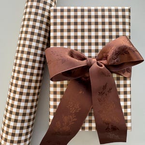May include: Brown and white gingham wrapping paper with a brown satin ribbon with a floral pattern. The ribbon is tied in a bow.