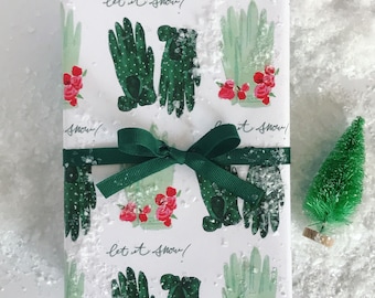 May include: White gift wrap with a green and white pattern of gloves and red roses. The text "Let it snow!" is repeated on the wrapping paper. A green ribbon is tied around the gift.