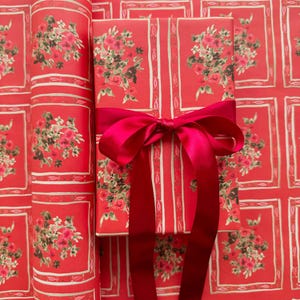 May include: Two red gift boxes with a floral pattern and white trim. The boxes are tied with a bright red satin ribbon.