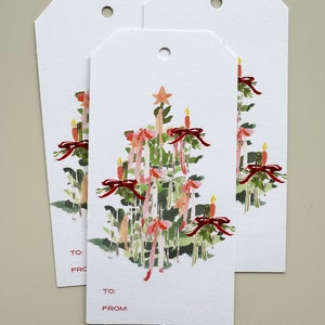 May include: Three white gift tags with a watercolor illustration of a Christmas tree with red bows, pink ribbons, and lit candles. The tags have the words "TO:" and "FROM:" printed on them.