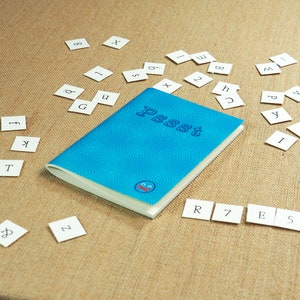 Pode incluir: Um caderno azul com a palavra "Pssst" escrita na capa. O caderno está rodeado de pequenos quadrados brancos com letras e números.