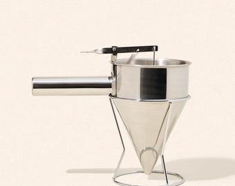 May include: A stainless steel funnel dispenser with a conical body, a horizontal handle, and a spring-loaded trigger mechanism. The device is supported by a wire stand with a circular base, designed for controlled pouring of batters or sauces.